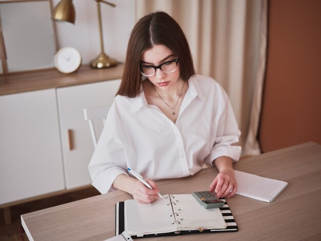 A girl writes something in a notebook while sitting at the table